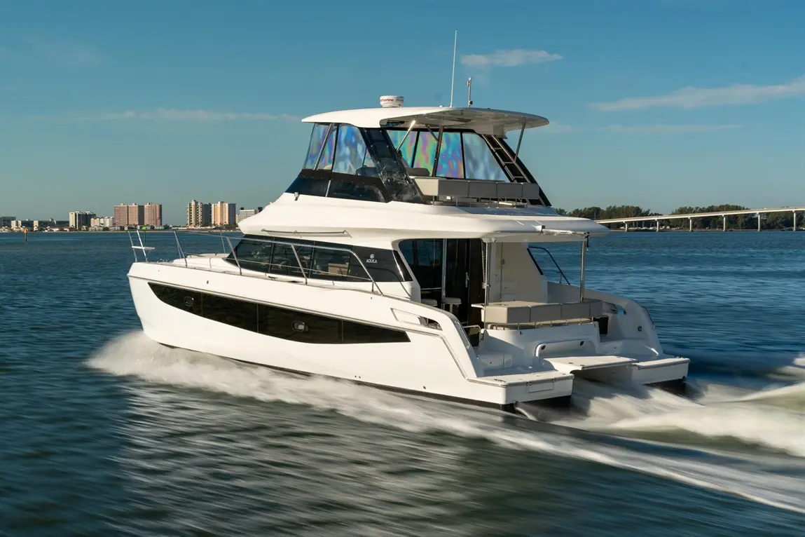 A sleek white powerboat glides through blue waters, with a city skyline in the background under a clear sky.